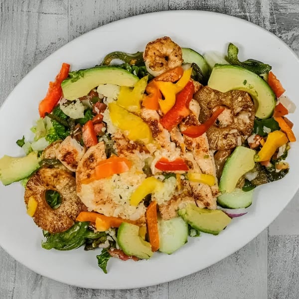 Grilled chicken and shrimp salad with avocado, bell peppers, and pineapple on a white plate.