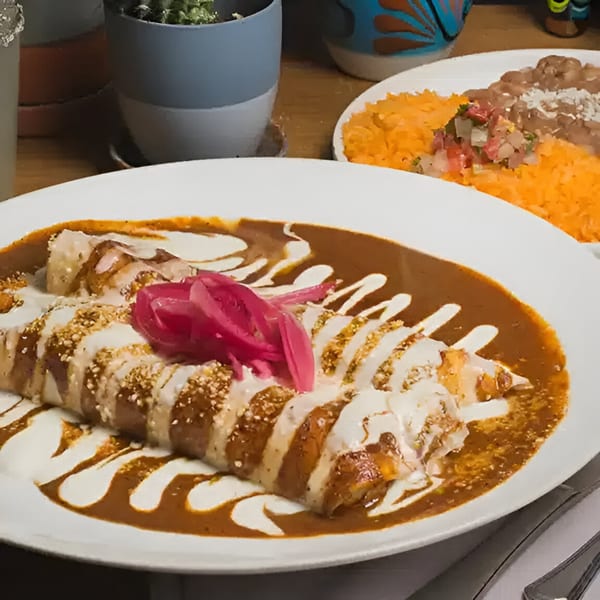 Mas Chingon enchiladas with mole sauce, crema, pickled onions, and a side of rice and beans.
