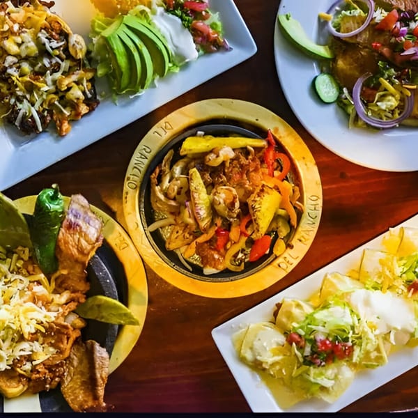An overhead view of four plates of Mexican food, including fajitas, enchiladas, and nachos.