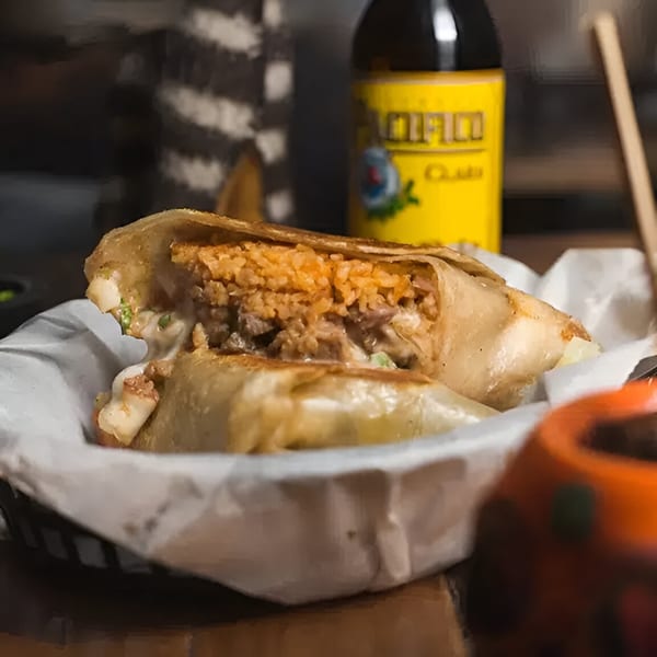 A large, cut burrito filled with rice, meat, and cheese, served in a basket with a drink.